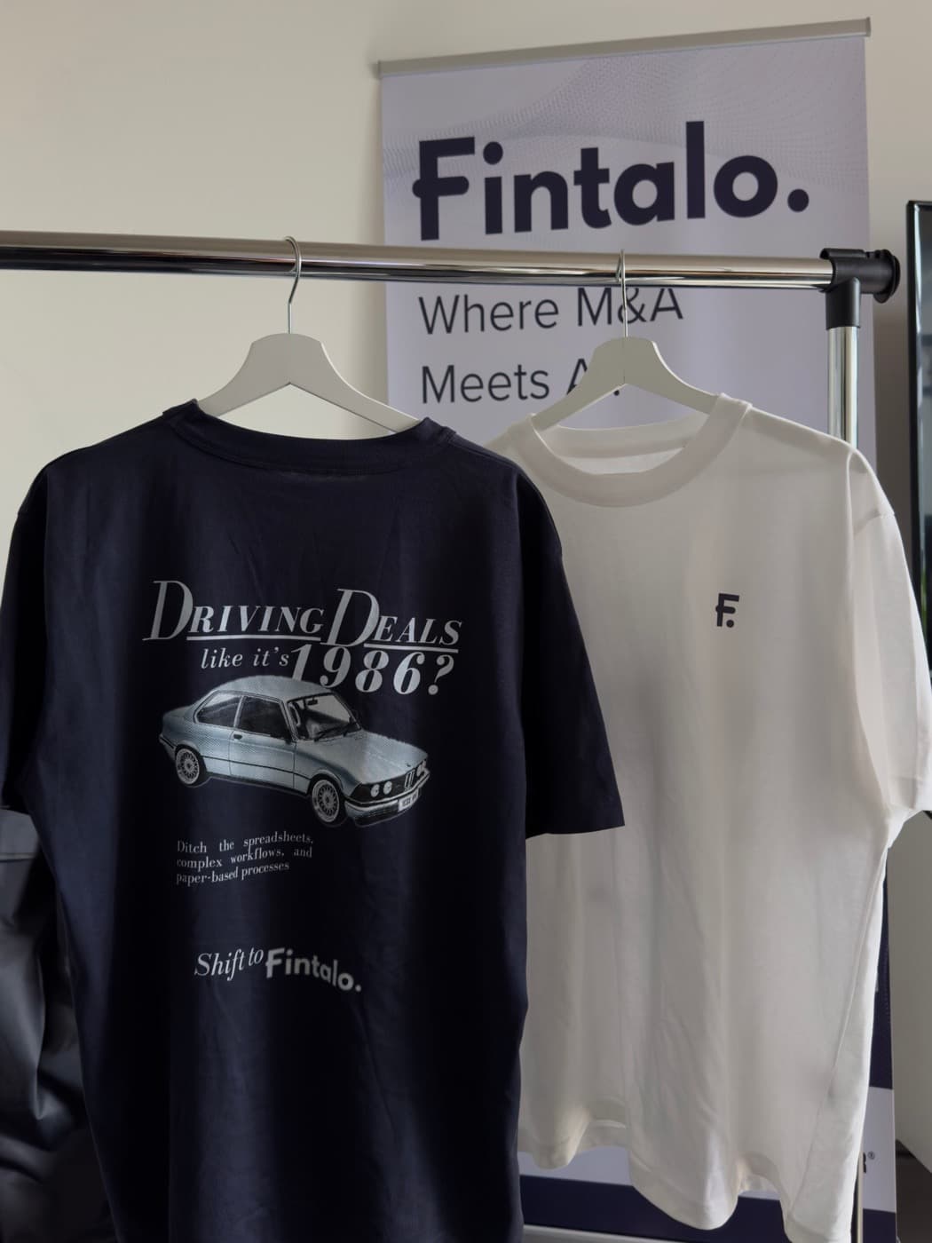 Two Fintalo-branded t-shirts hanging on a rack in front of a Fintalo banner